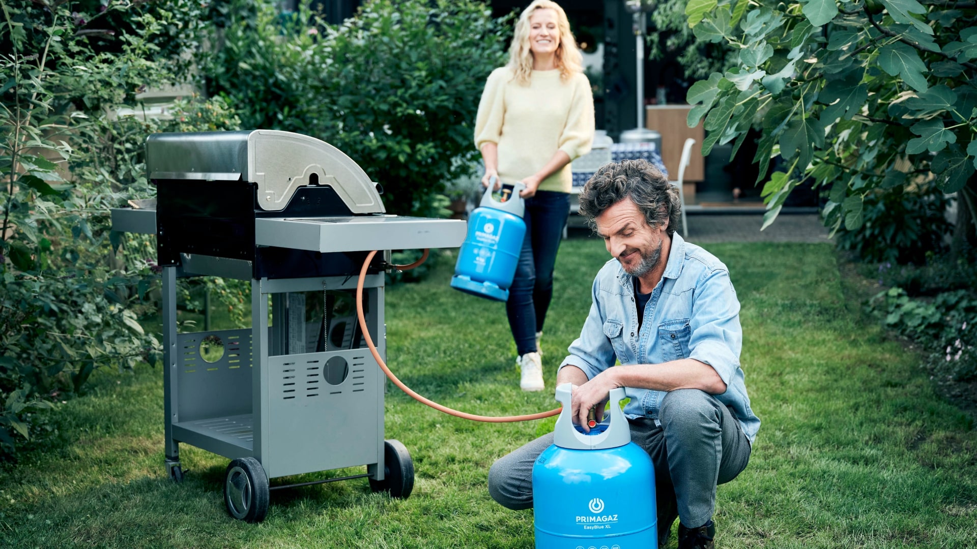 2 mensen sluiten gasfles aan op een barbeque in een tuin