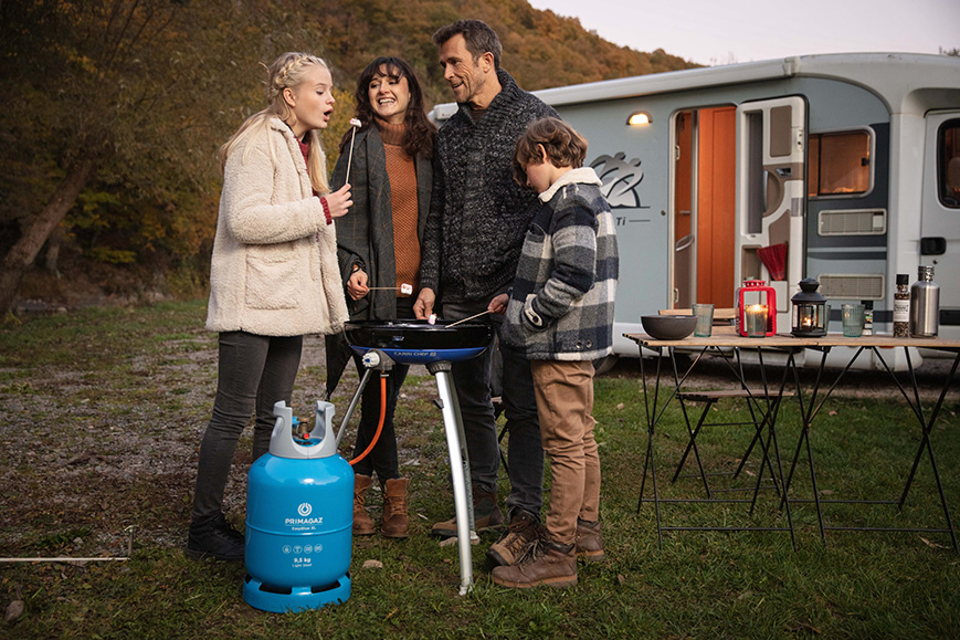 Gasfles aangesloten op barbeque op een camping met familie eromheen